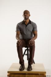 Sitting reference of whole body black white striped shirt brown jeans brown shoes Arturo